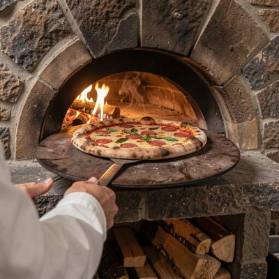 a wood fired pizza being pulled from a stone oven