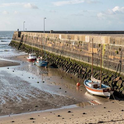 a harbour wall with boats at low tide