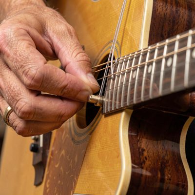a hand adjusting the tuning pegs of a guitar