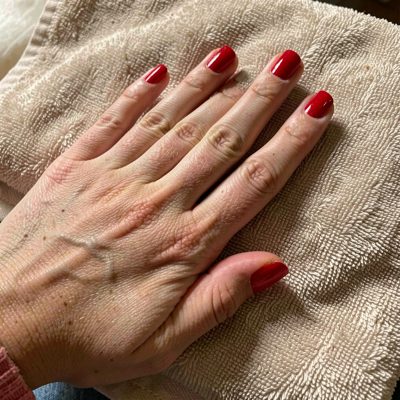 a hand with freshly painted red nails resting on a towel