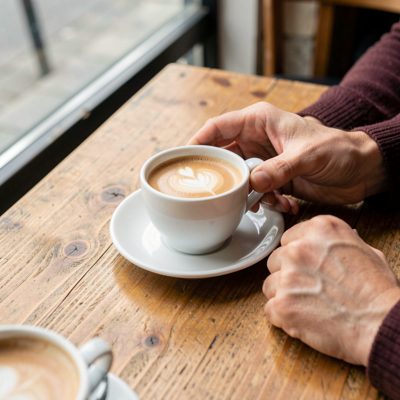 hands holding a coffee cup across a table