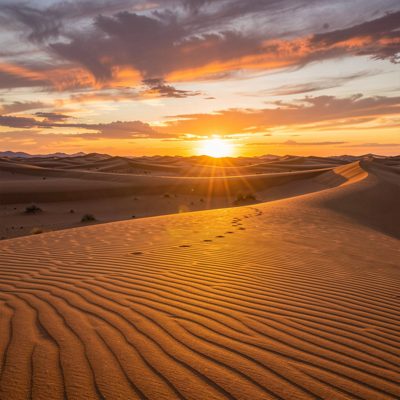 a desert sunset with long shadows across the sand