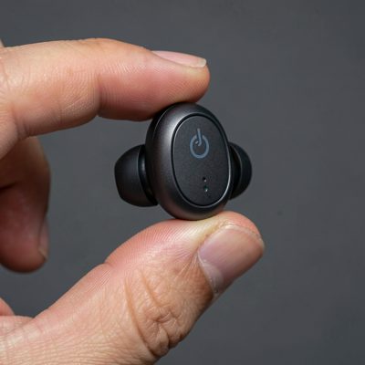 a single wireless earbud held between finger and thumb