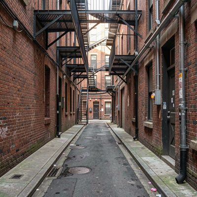 a narrow lane with fire escapes overhead
